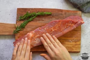 patting seasoning down on raw pork tenderloin