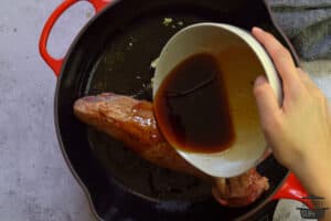 pouring sauce over pork tenderloin in pan