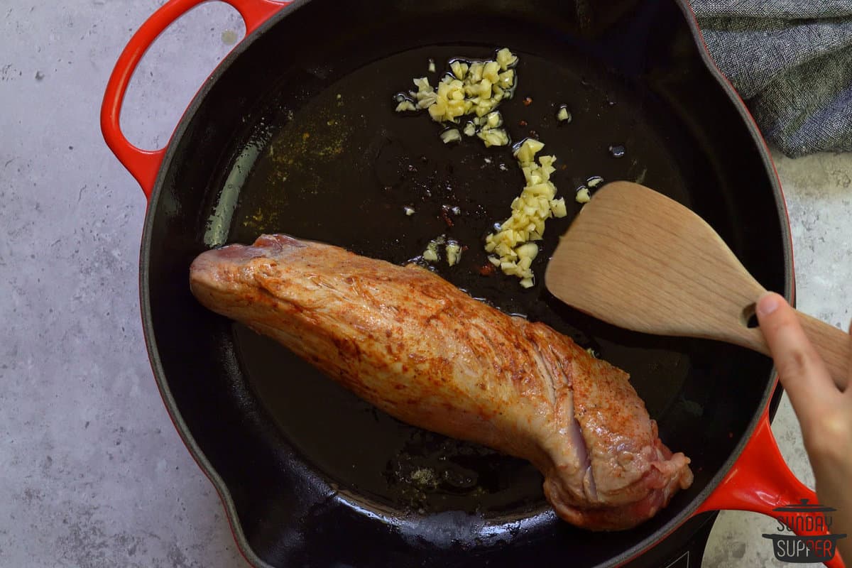 cooking garlic in pan next to pork tenderloin