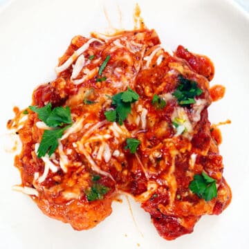 chicken parmesan on a white dinner plate with a topping of parsley