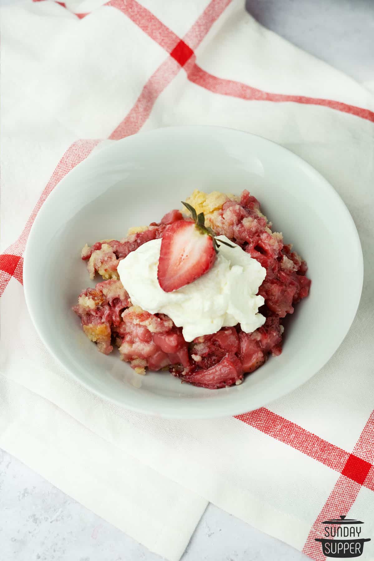 a serving of strawberry dump cake in a bowl with whipped cream and a strawberry on top