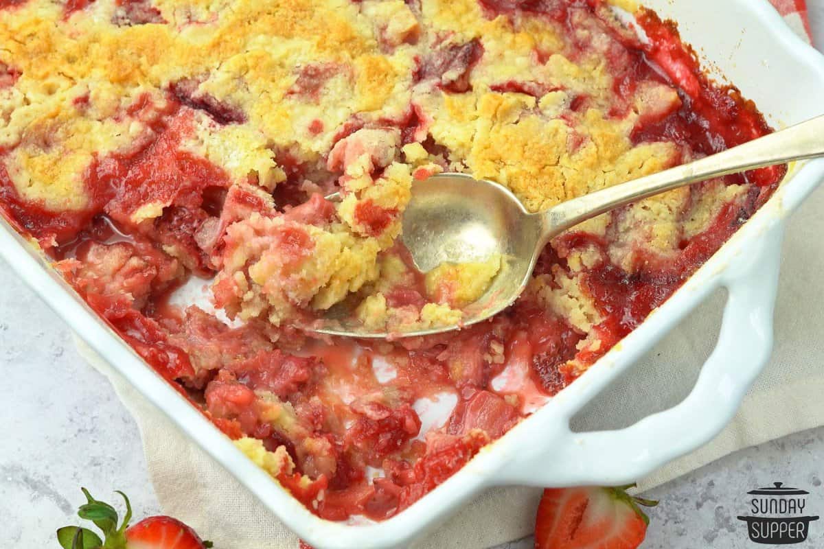 a large serving spoon in a white dish of strawberry dump cake