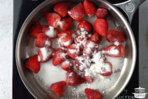 frozen strawberries in a metal saucepan with sugar and cornstarch