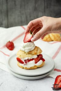 adding a strawberry to the top of a shortcake on a plate