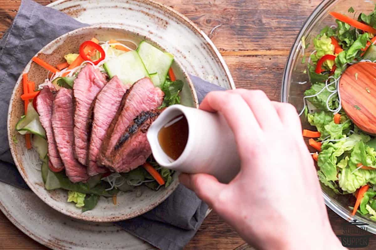 pouring salad dressing over Vietnamese steak salad in a bowl