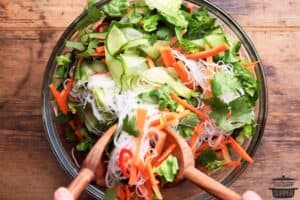 Tossing rice noodles with Vietnamese beef salad ingredients using tongs