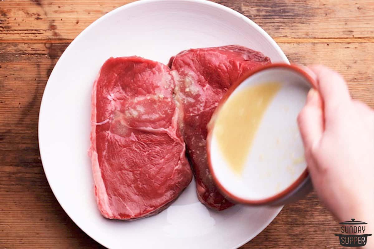 Pouring Vietnamese beef marinade over sirloin steaks on a white plate