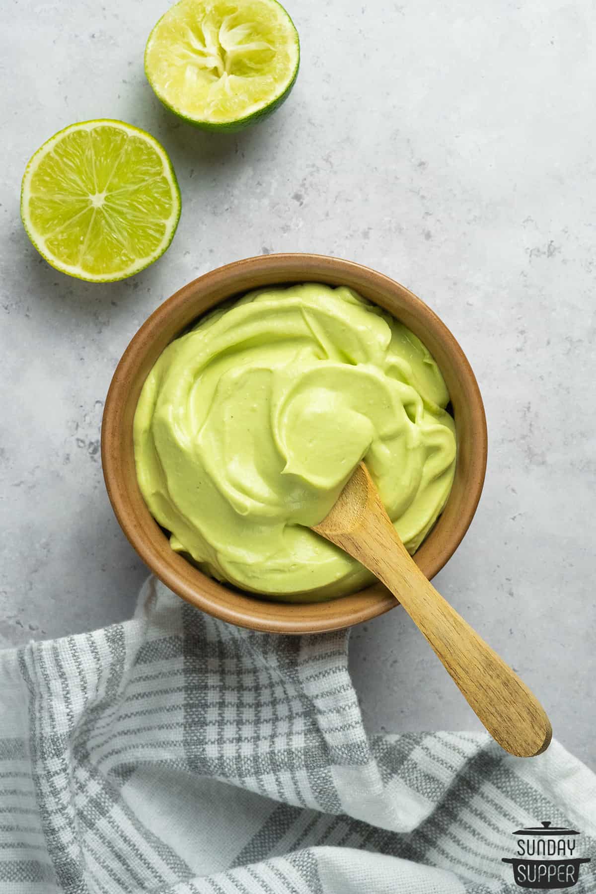 avocado crema in a wooden bowl with a wooden spoon next to two lime halves