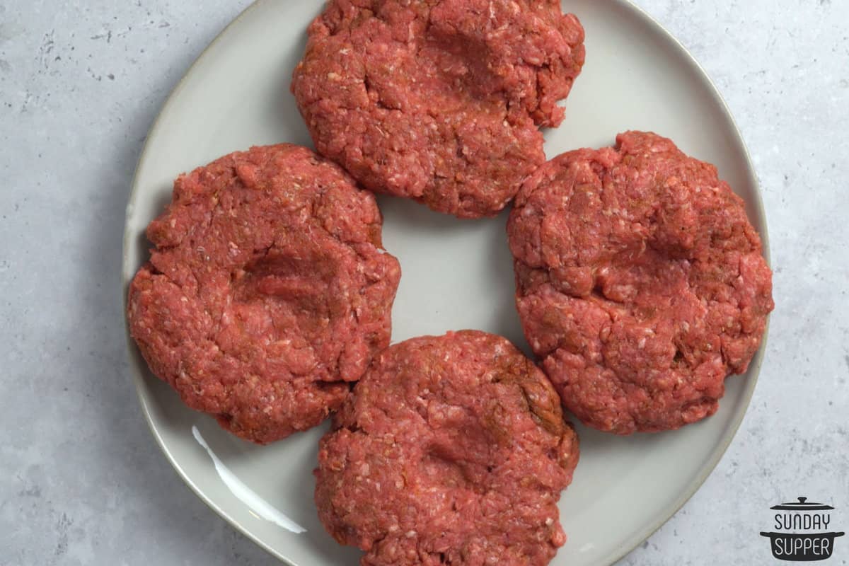 four burger patties with thumb depressions in the middle