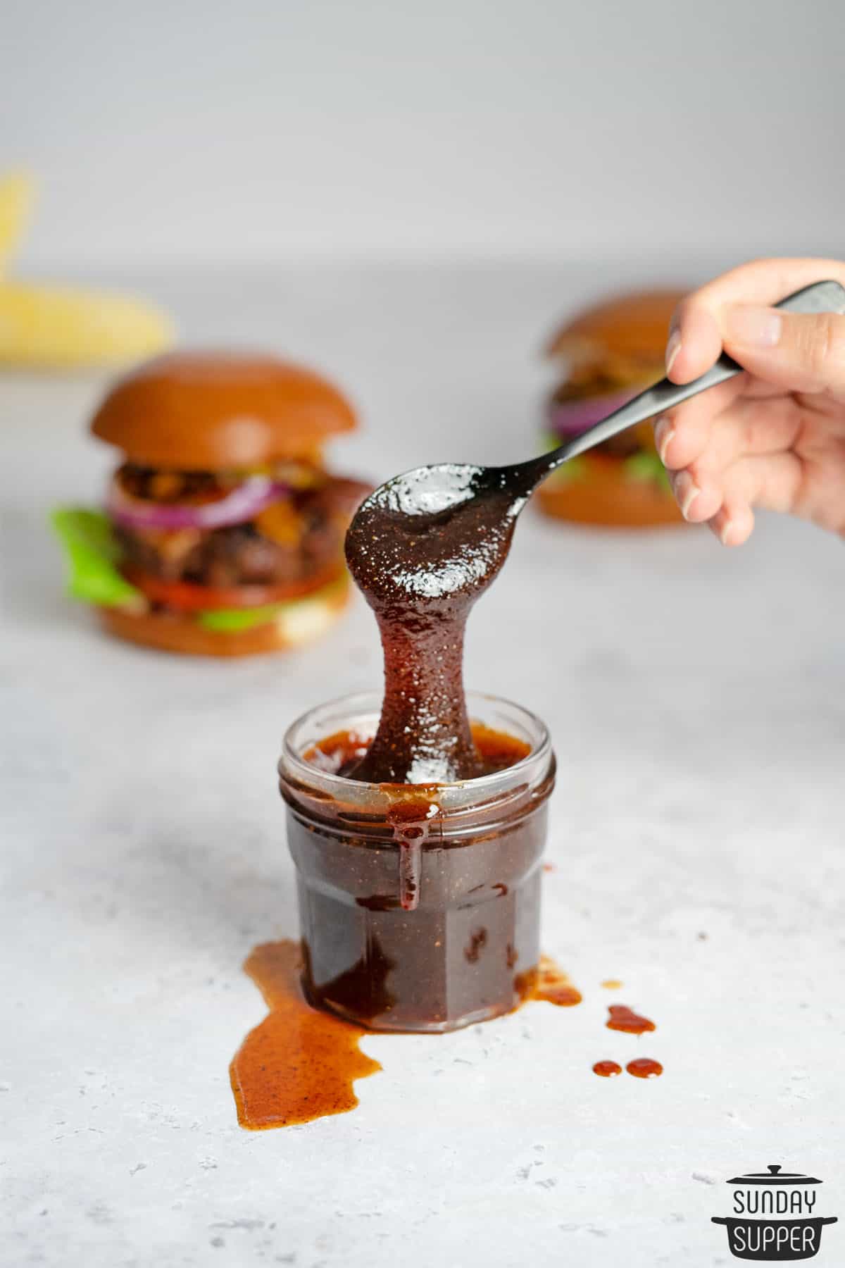 bbq sauce in a clear jar with a spoon dripping sauce down