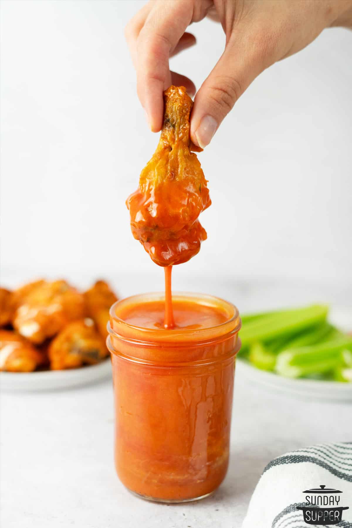 chicken wing dipping into a mason jar full of buffalo sauce