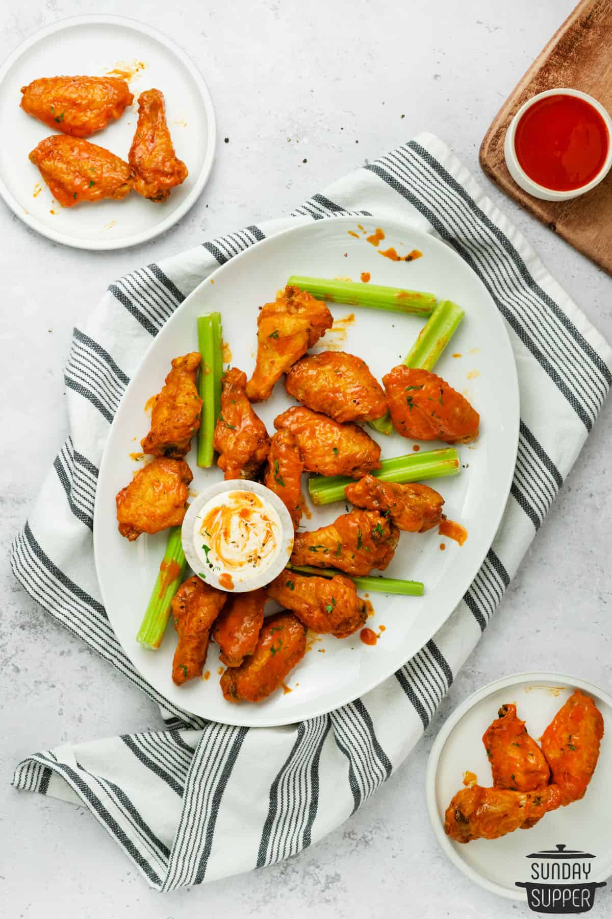 buffalo chicken wings on a white plate with buffalo sauce on the side