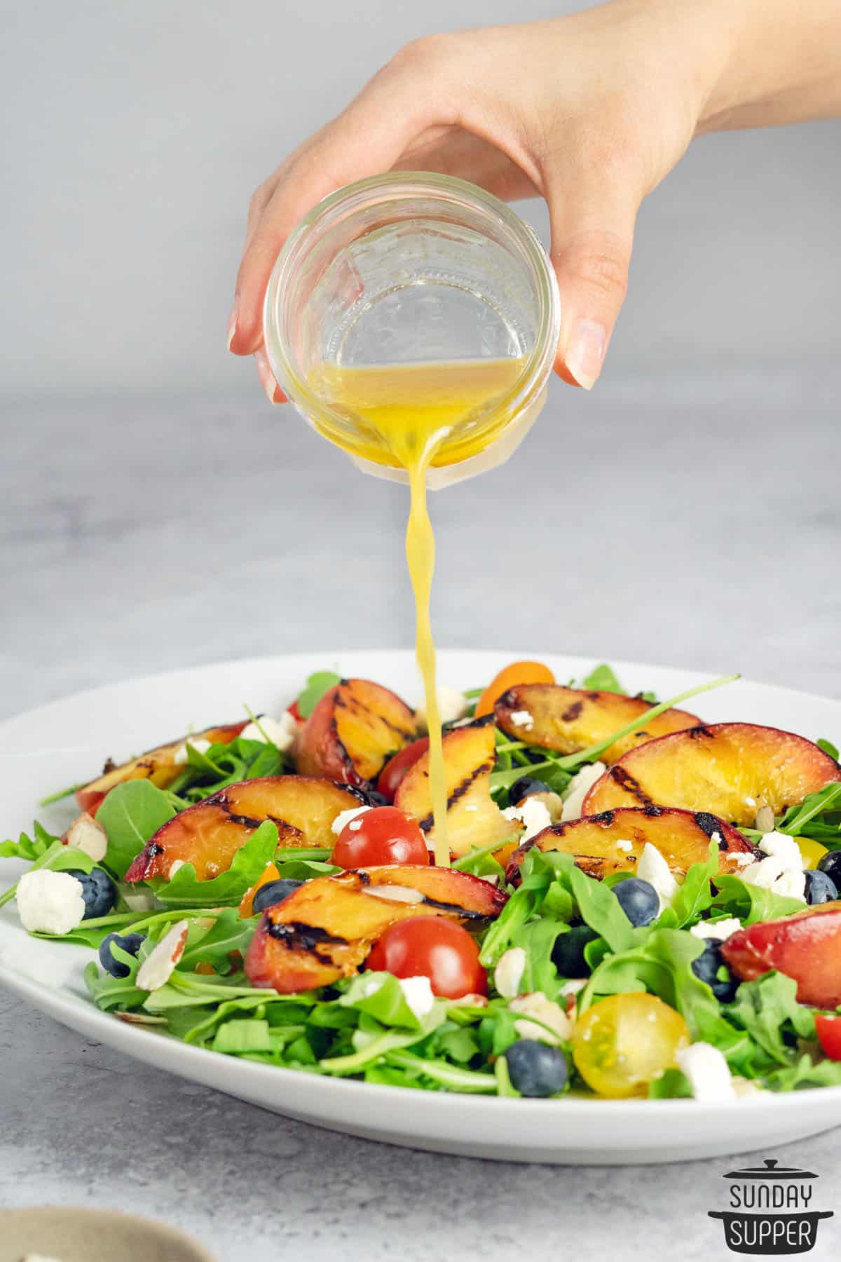 pouring dressing on a grilled peach salad