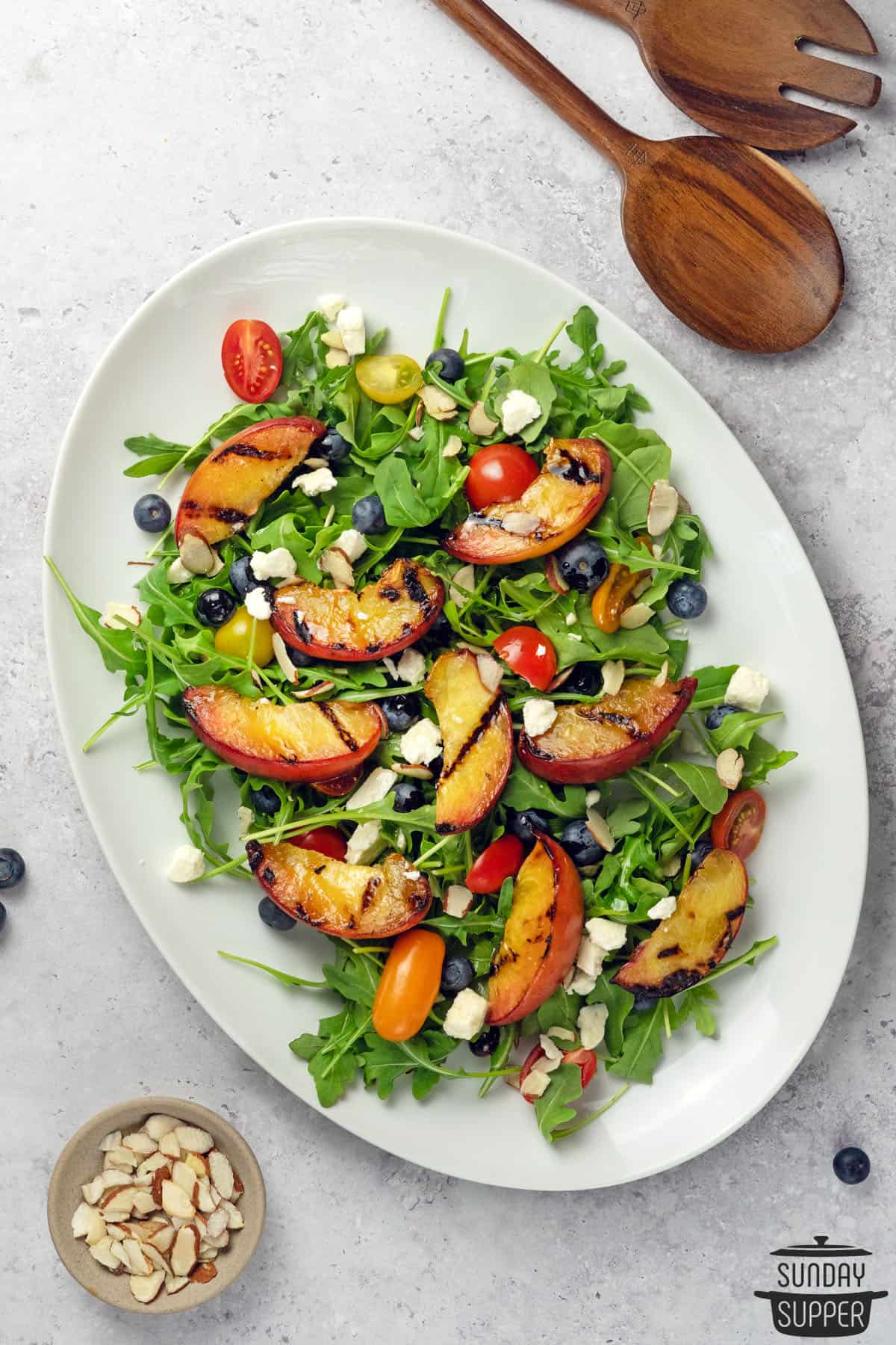 grilled peach salad on a white plate with almonds and salad utensils on the side