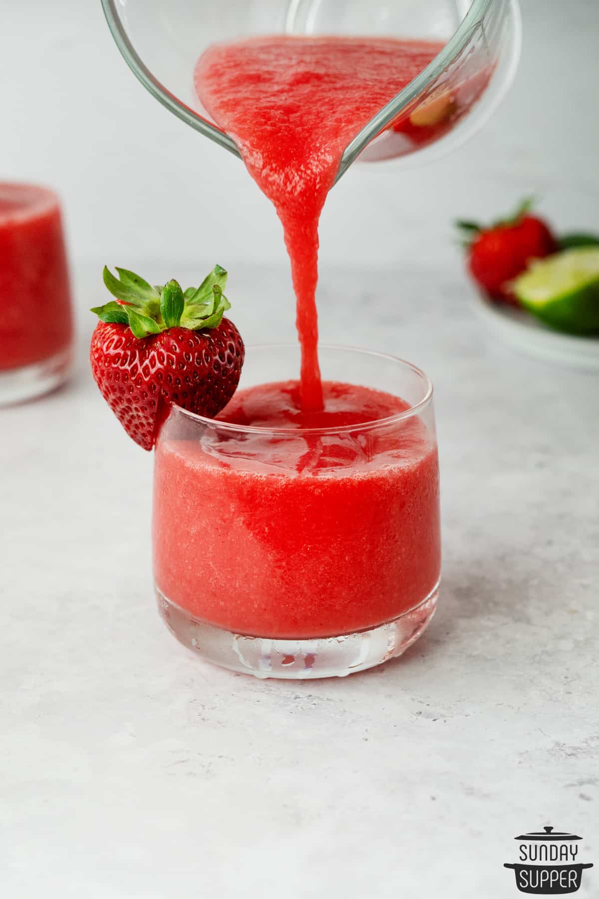 pouring strawberry daiquiri into a clear glass