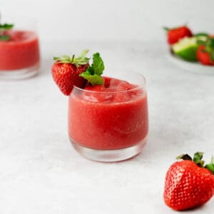 strawberry daiquiri in a clear glass with strawberry and mint on the rim