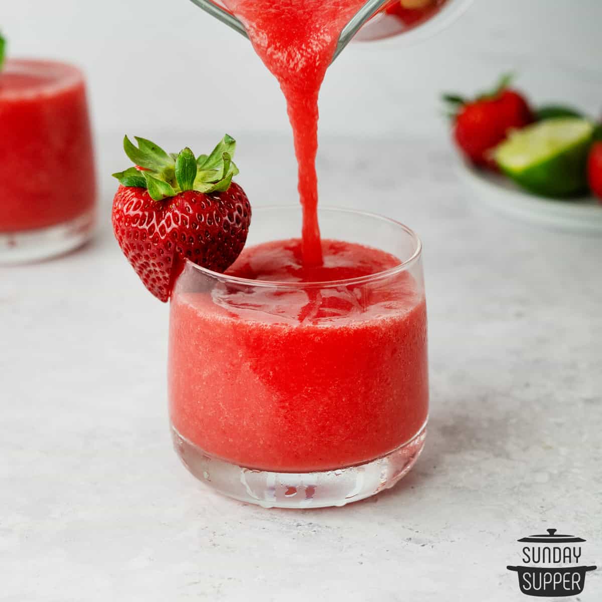 pouring strawberry daiquiri in a clear glass with a strawberry on the rim