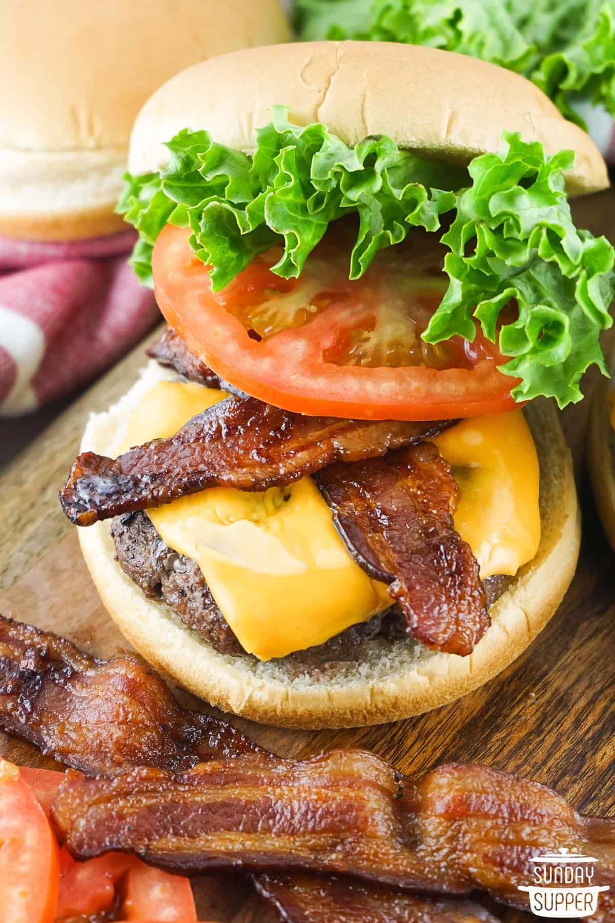 a wagyu burger on a cutting board with bacon, cheese, tomato, and lettuce