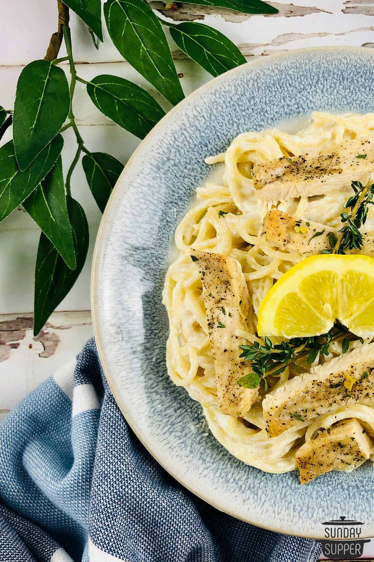 completed lemon ricotta pasta with chicken in a blue bowl with a serving towel and a plant