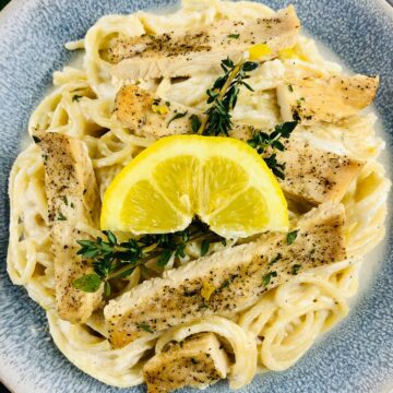 a bowl of ricotta chicken pasta with a lemon wedge and thyme