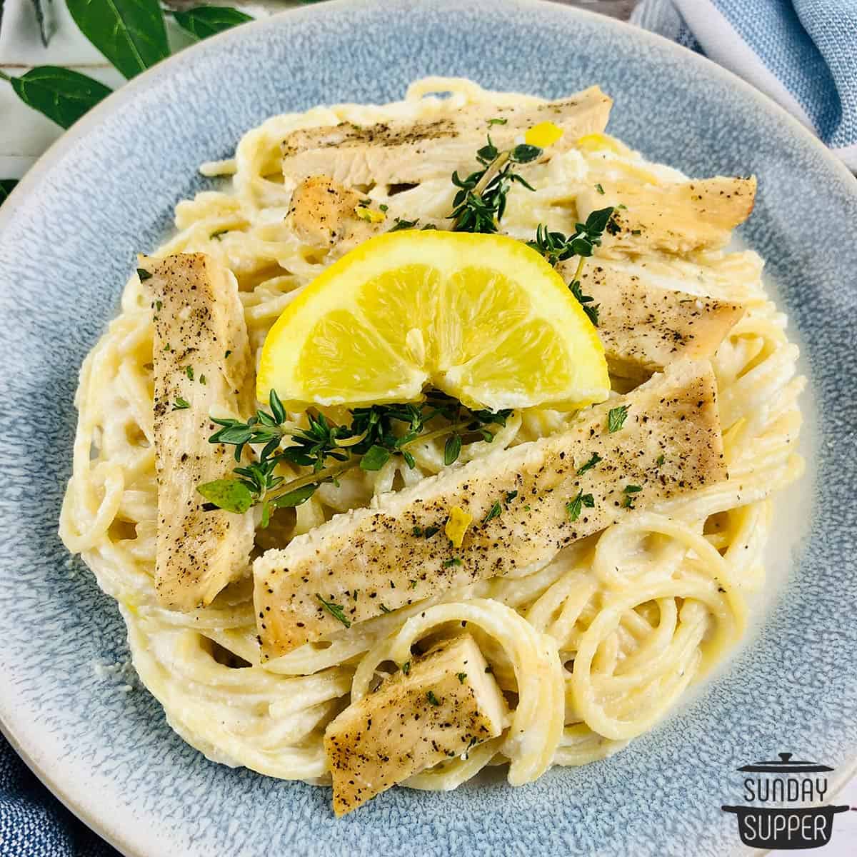 a bowl filled with lemon ricotta chicken pasta with a lemon wedge and fresh thyme