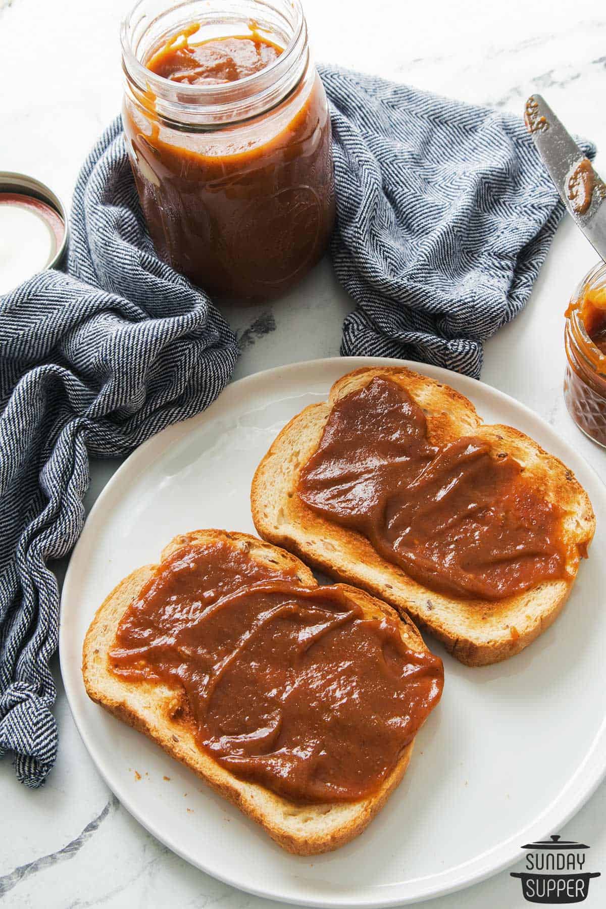 a plate with two pieces of toast coated in pumpkin butter, with a jar of pumpkin butter in the background