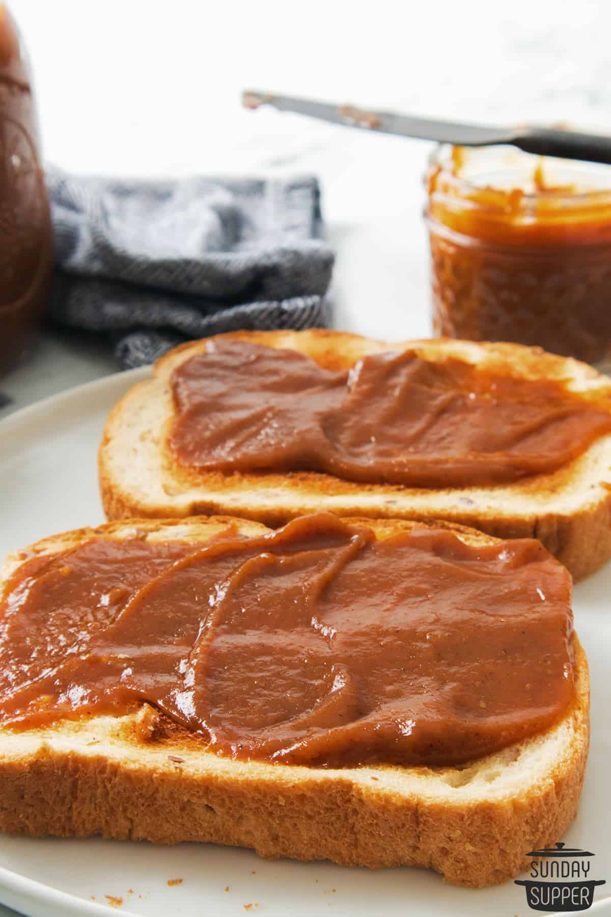 two pieces of toast spread with pumpkin butter with a jar of pumpkin butter in the background