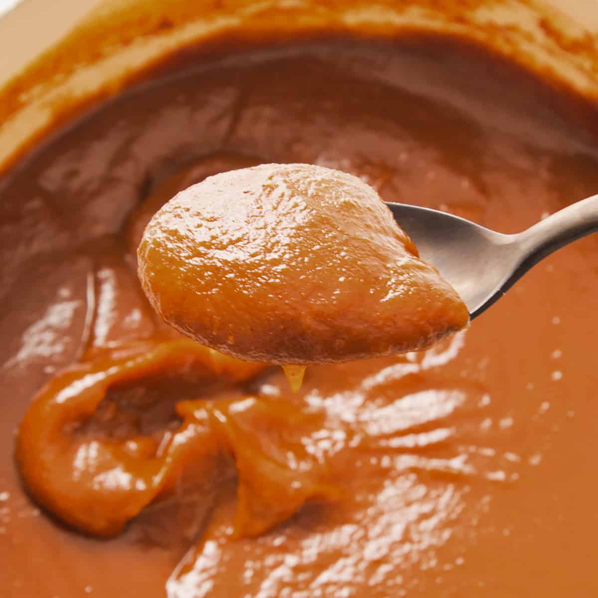 a spoon full of pumpkin butter over a pot full of more pumpkin butter