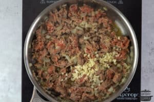 adding garlic to pan with sausage and onions