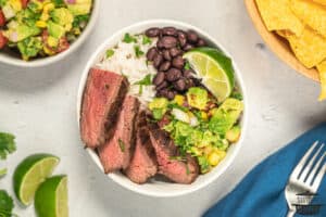 flank steak sliced in a rice bowl with beans, avocado salsa, and lime