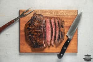 sliced flank steak on a cutting board with a steak fork and knife