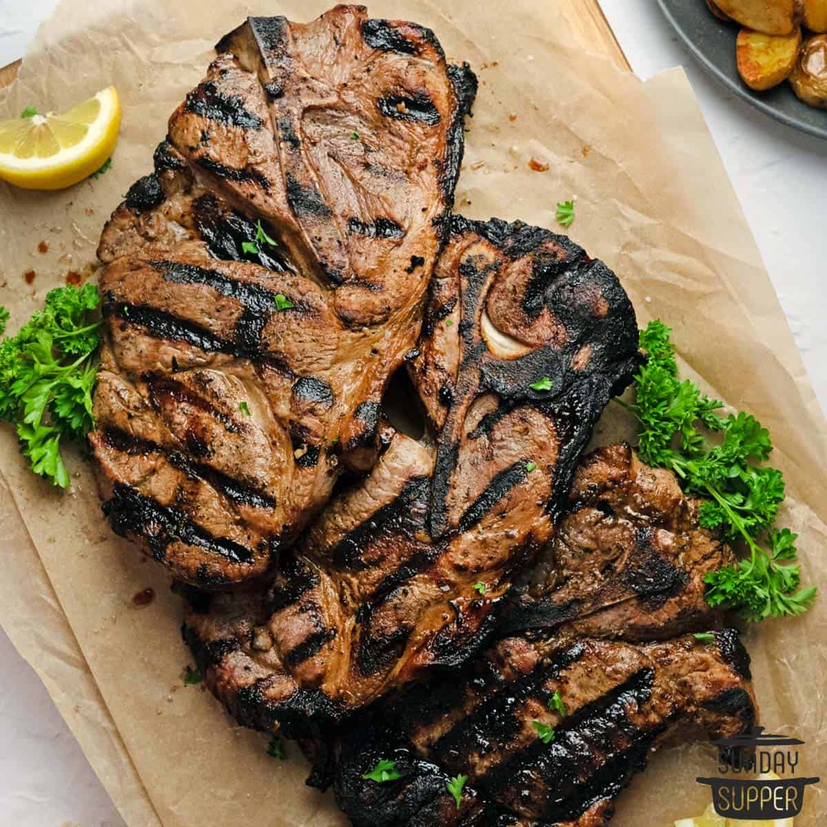 three grilled pork steaks on butcher paper with lemons and parsley
