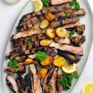 sliced pork steaks on a serving platter with potatoes and parsley