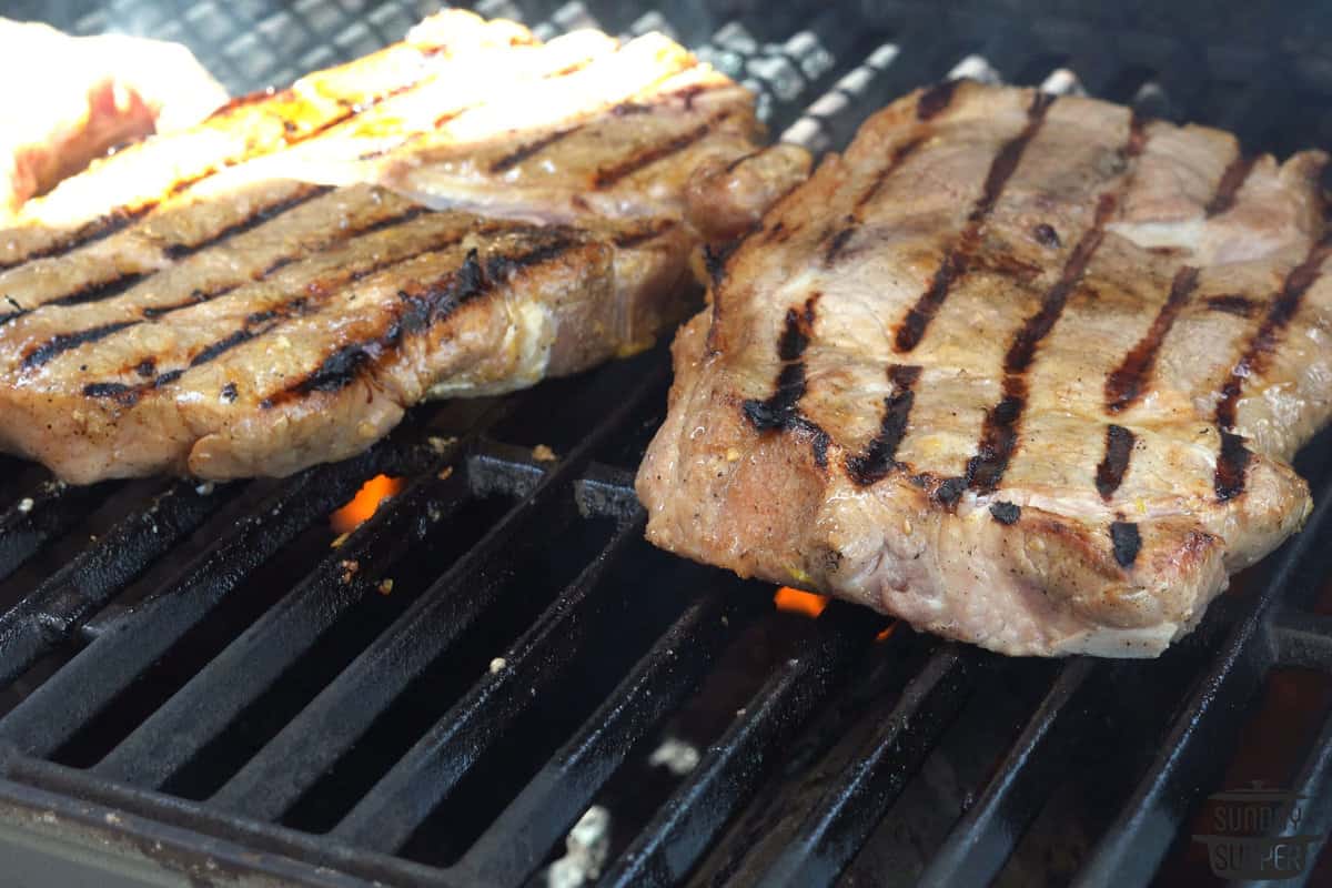 pork steaks cooking on a grill with char marks on one side
