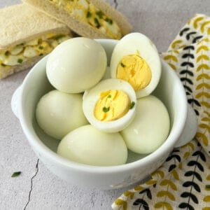 a bowl filled with hard boiled eggs next to egg salad sandwiches