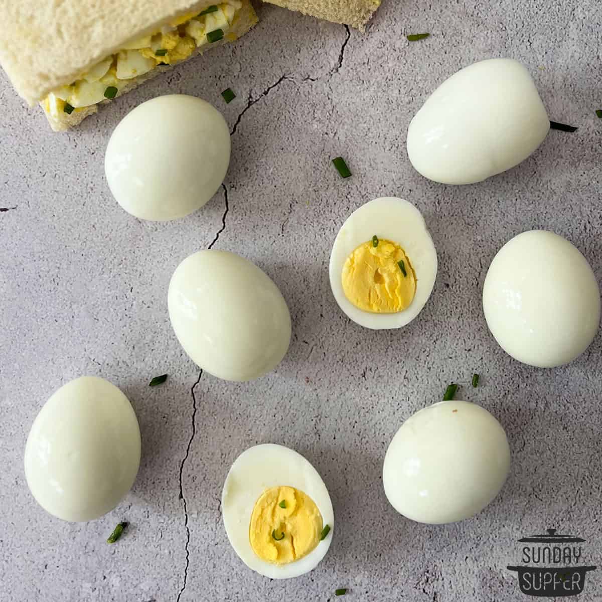 sliced and whole hard boiled eggs on a counter with a sandwich and chives