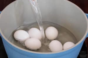 cold water being poured into the pot of eggs
