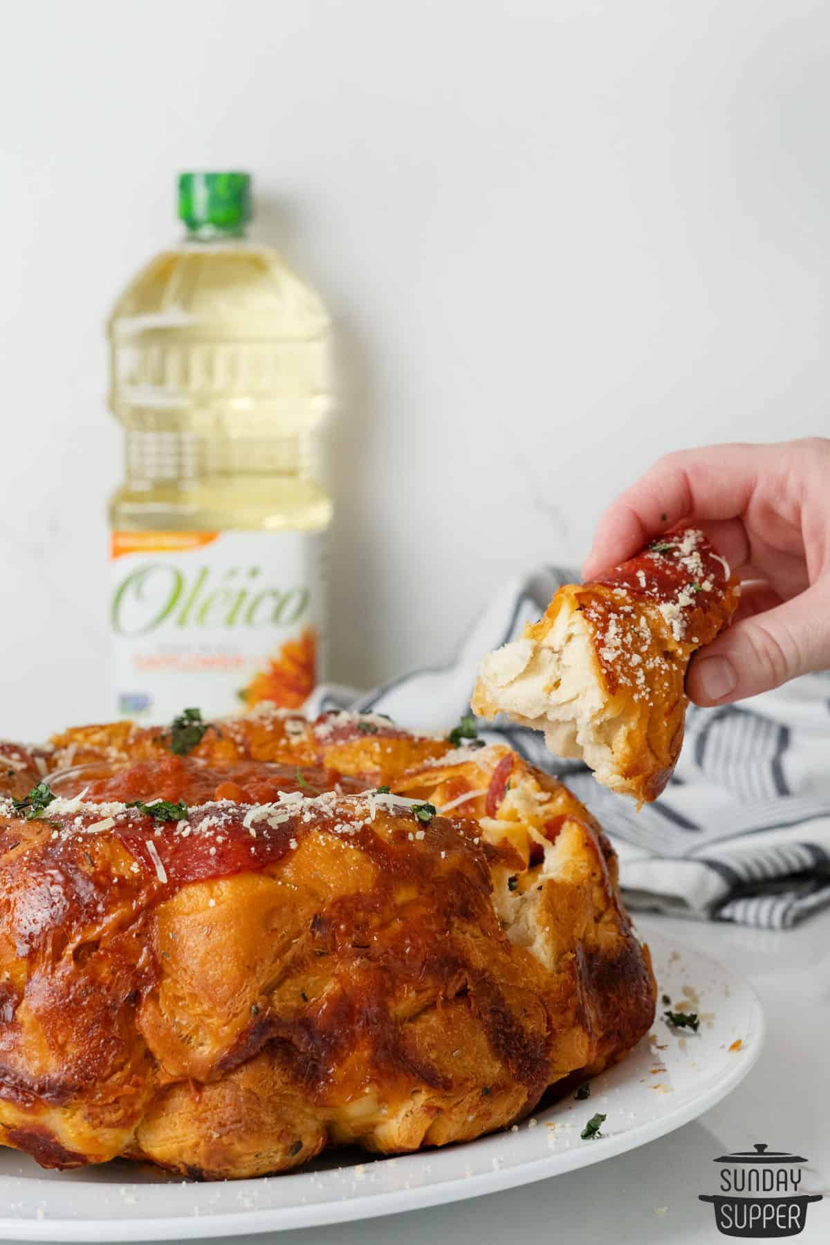 pulling a piece of pizza monkey bread away from the plate in front of a bottle of Oléico® safflower oil