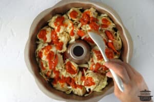 adding marinara sauce to bundt pan with biscuit dough
