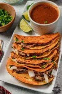 quesabirria tacos on a white platter with birria consome in a ramekin