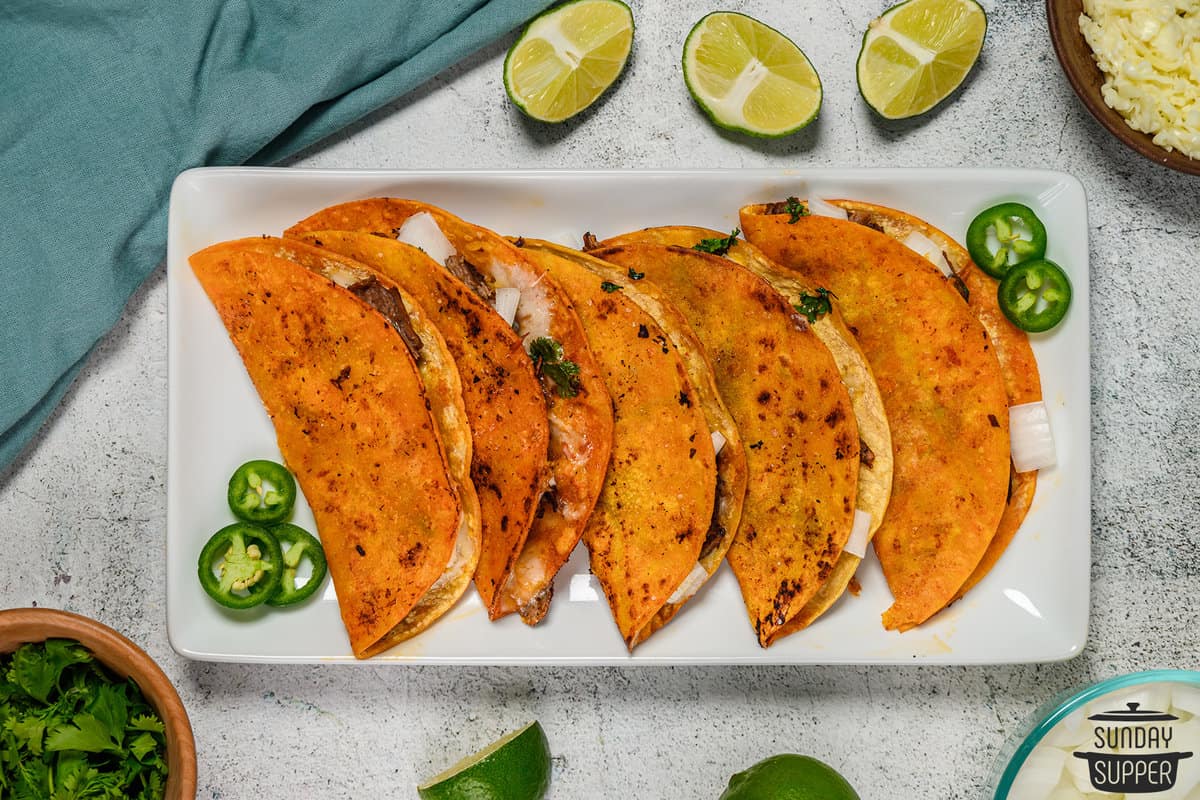 five quesabirria tacos on a platter with jalapeno slices