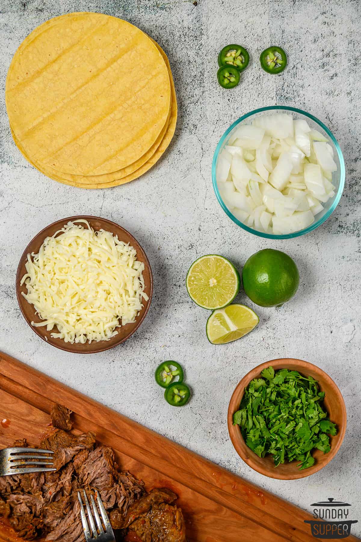quesabirria toppings: onions, cilantro, limes, cheese, and tortillas on a table