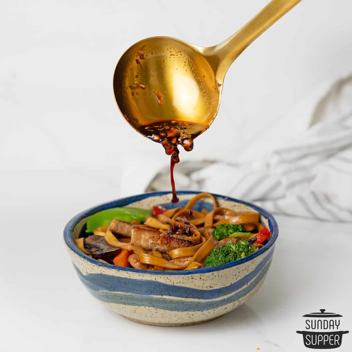 drizzling teriyaki sauce over a bowl of noodle stir-fry