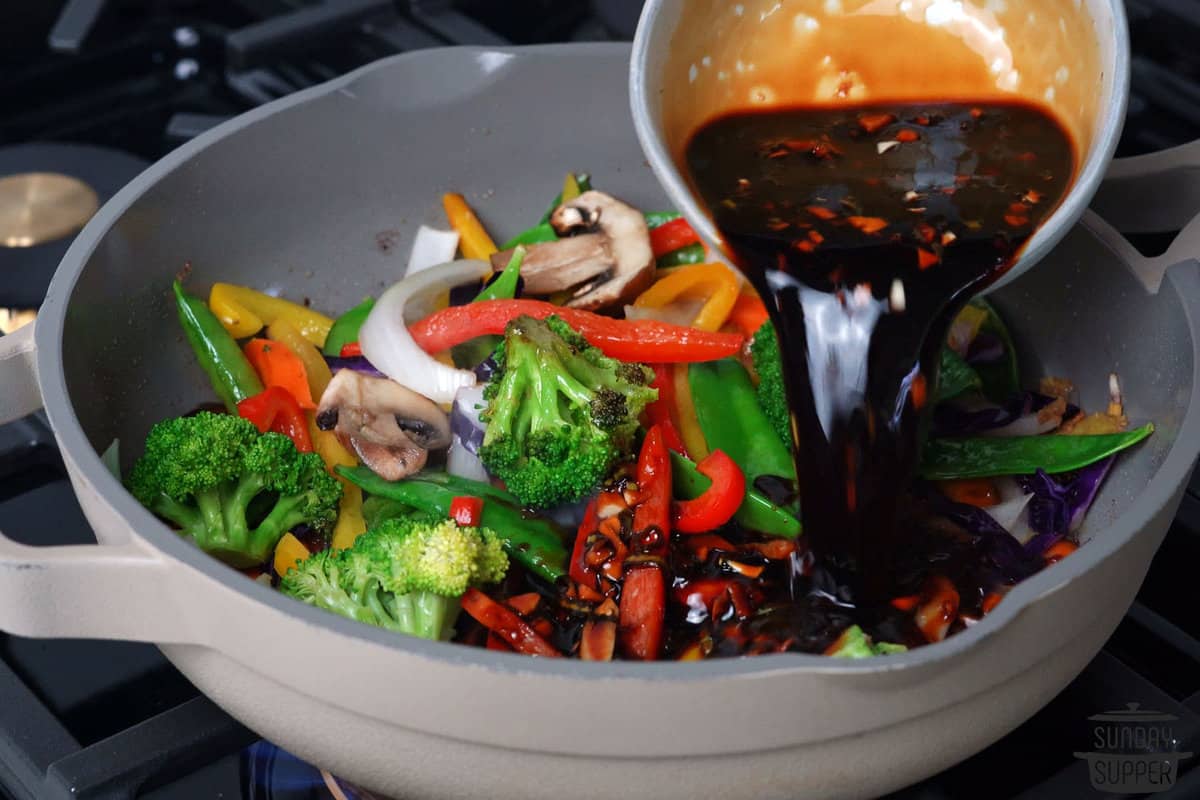pouring teriyaki sauce into a pan with stir-fry