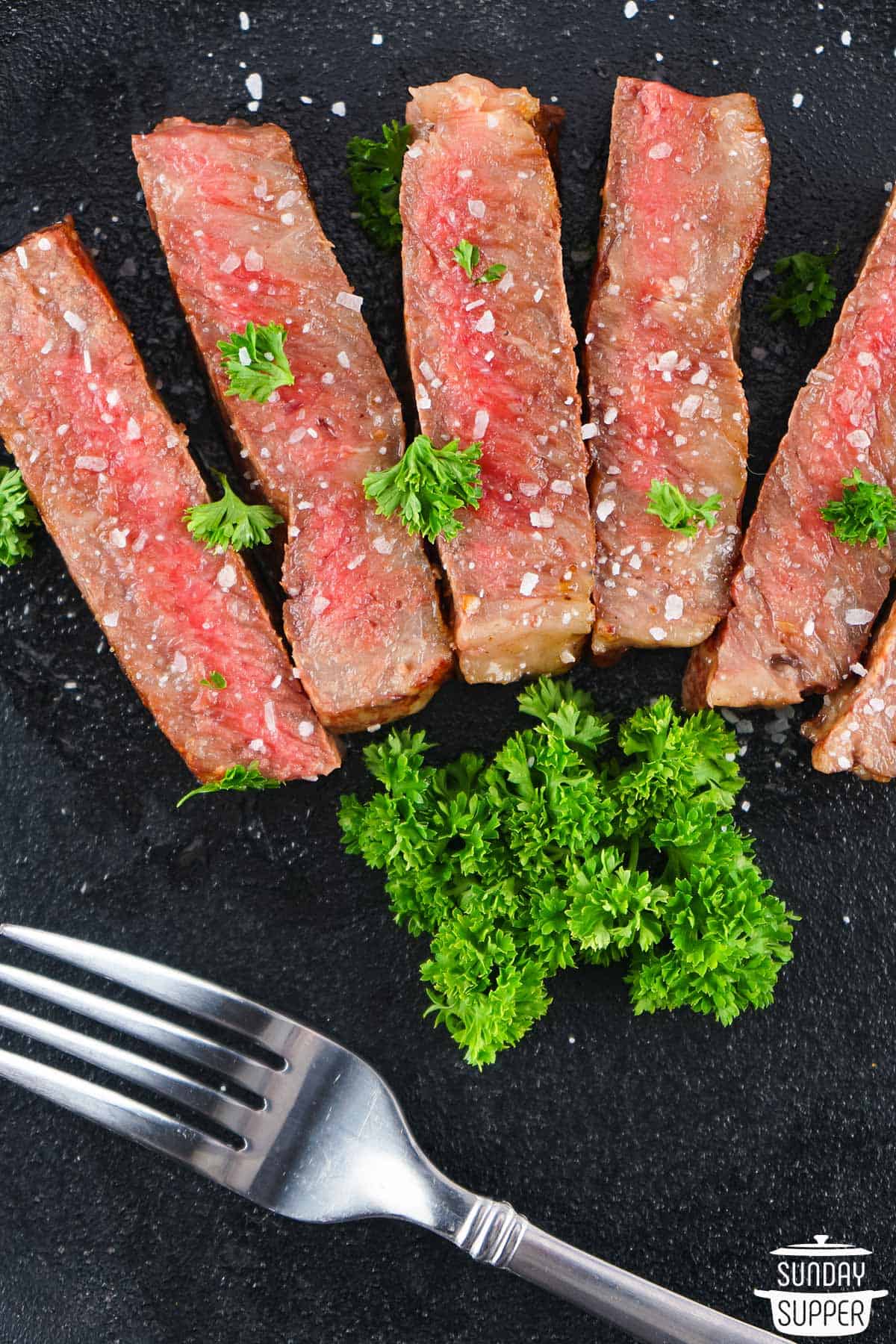 slices of wagyu steak on a black pan with parsley and a fork