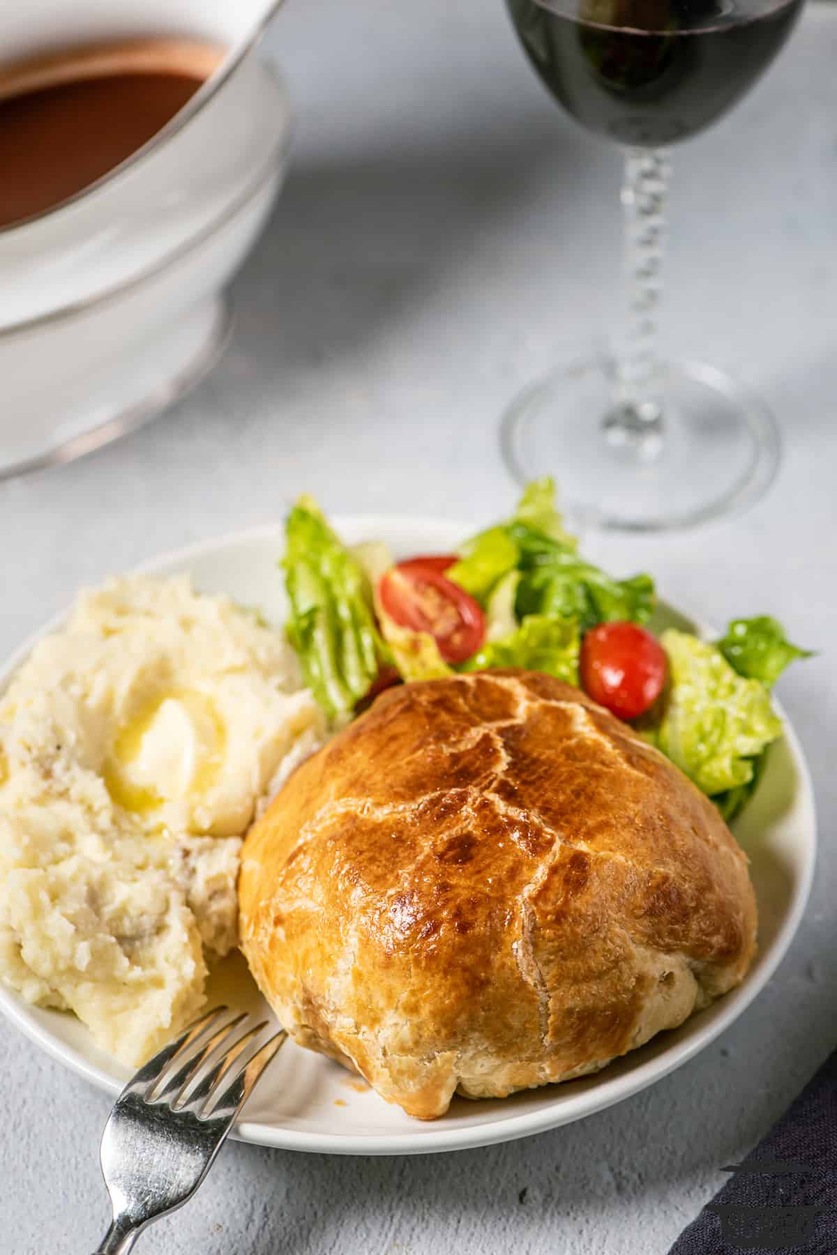 beef wellington on a plate with mashed potatoes and salad