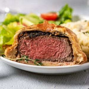 beef wellington sliced on a plate with fresh herbs