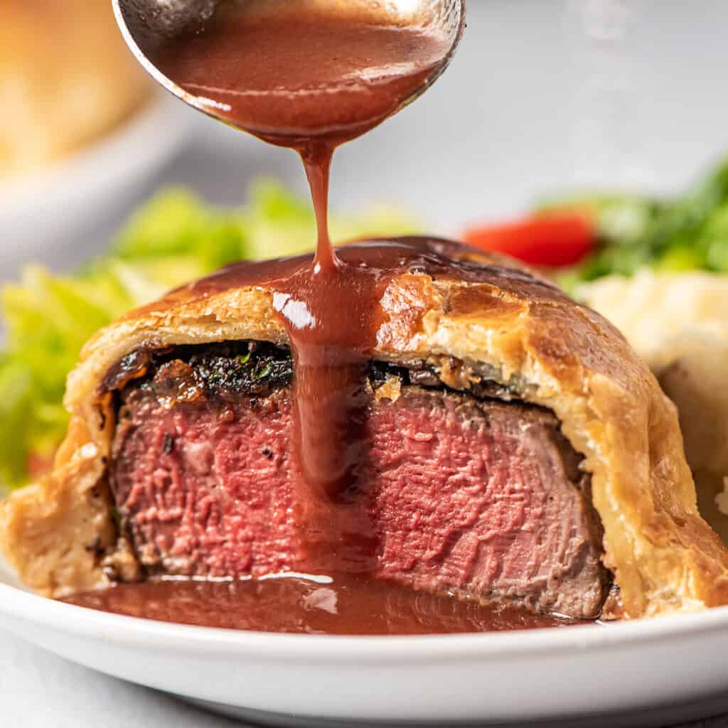 pouring espagnole sauce over beef wellington on a plate