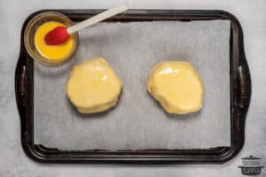 brushing beef wellingtons on a baking sheet with egg wash to bake