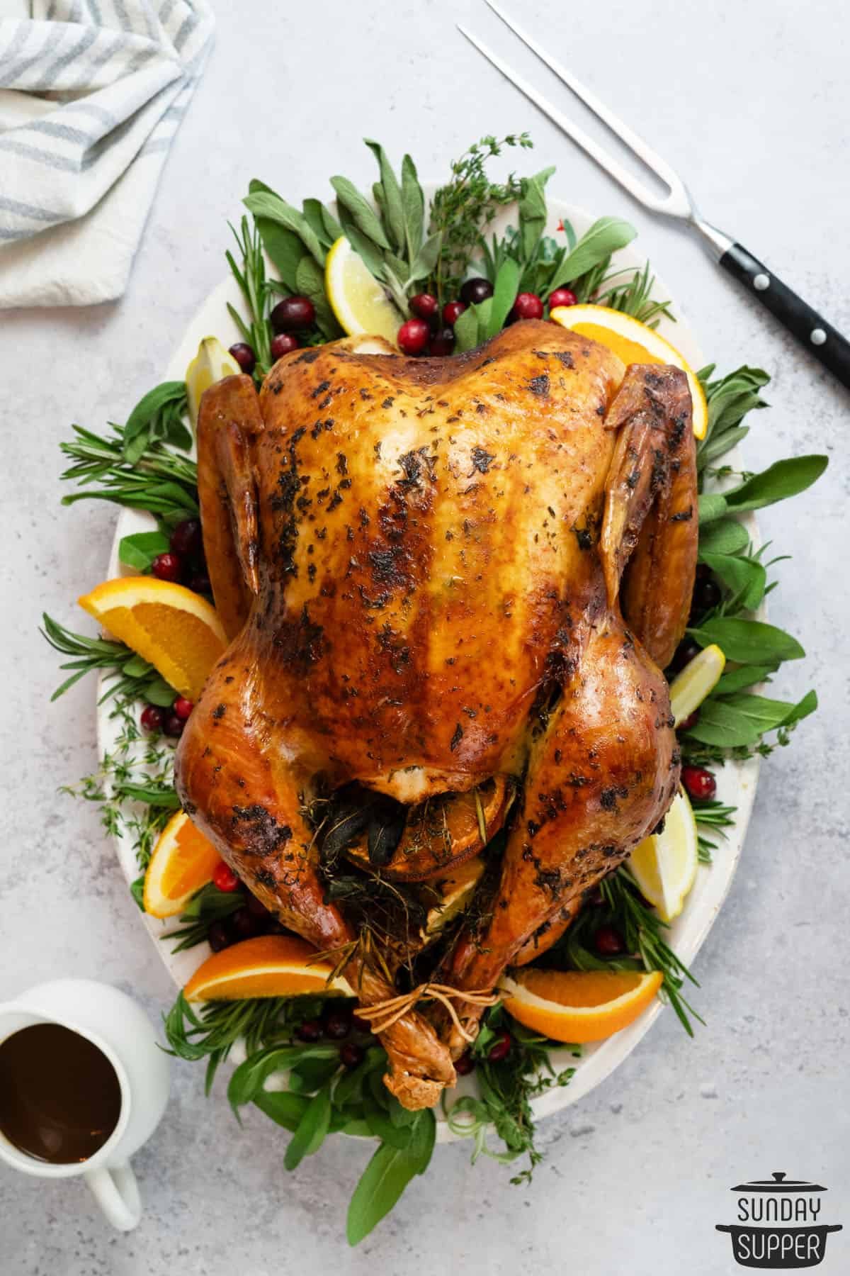 whole thanksgiving turkey on a platter with orange wedges and greens